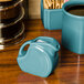 A turquoise Fiesta disc china creamer pitcher on a wood surface.