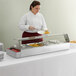 A woman in a white coat serving food from an Avantco countertop buffet warmer.