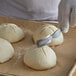 A person using a Mercer Culinary bread lame to score dough on a counter.