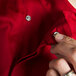 A person's fingers adjusting hidden snap buttons on a tomato red Chef Revival chef jacket.