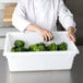 A chef in a white coat putting green peppers in a white Rubbermaid food storage container.