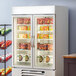 A Beverage-Air white glass door merchandiser freezer with shelves full of food.