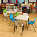A white square Lifetime children's table in a classroom with green and blue chairs.