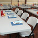 A Lifetime professional-grade plastic folding table set with white chairs and glasses on it.