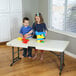A boy and girl playing with colorful plastic blocks on a Lifetime almond plastic folding table.