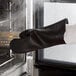 A person wearing black RITZ silicone oven mitts using them to remove something from an oven.