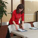 A woman in a red shirt putting a piece of paper on a Lifetime almond plastic folding table.