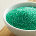 A bowl of light green sanding sugar on a wooden table.