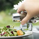 A person holding a Libbey salt shaker over a salad.
