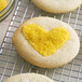 Heart shaped cookies with yellow sanding sugar on a cooling rack.