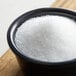 A bowl of Clear White Sanding Sugar on a wood surface.