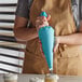 A person in an apron using an Ateco blue thermoplastic pastry bag to decorate a cupcake.