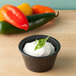 A white ramekin filled with white sauce and green onions in front of red and green peppers.