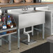 A Regency stainless steel underbar sink with a left drainboard on a counter with bottles of liquid in it.
