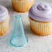 A cupcake with purple frosting and a blue cone with a plain piped swirl on top.
