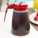 A Tablecraft red polypropylene syrup dispenser with a red lid.