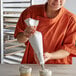 A woman in an orange shirt using an Ateco polyurethane coated cotton pastry bag to frost a cupcake.