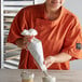 A woman in an orange shirt using an Ateco Wunderbag to frost a cupcake.