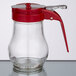 A Tablecraft glass teardrop syrup dispenser with a red lid.