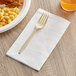 A plastic fork on a white Choice dinner napkin next to a plate of macaroni and cheese.