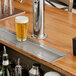 A Regency stainless steel beer drip tray on a bar counter with a drain.