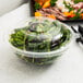 A Fineline clear plastic bowl filled with salad with a clear lid.