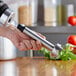 A hand holding a Galaxy light-duty immersion blender shaft over a table with tomatoes.