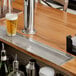 A Regency stainless steel flush mount beer drip tray on a bar counter with a glass of beer and foam.