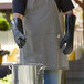 A man wearing black San Jamar neoprene gloves and an apron pouring liquid into a pot.