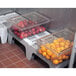 A Cambro slotted dunnage rack with several plastic containers of apples and oranges on it.