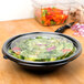 A bowl of salad with a clear flat lid on a table.