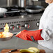 A woman chef using a San Jamar puppet style oven mitt to hold a flaming pan.