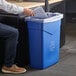 A person sitting at a desk in a corporate office putting papers in a blue Carlisle Trimline rectangular recycle bin.