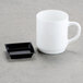 A white mug and black square dish on a table.