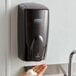 A person's hand using a black Rubbermaid Autofoam soap dispenser.