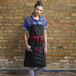 A woman wearing a black Uncommon Chef Rebel Bib Apron with red webbing.
