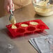 A person using a red Thunder Group silicone mold to pour batter into a muffin pan.