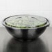 A Sabert black round bowl filled with salad and topped with a plastic lid.