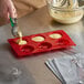 A person pouring batter into a Thunder Group red silicone savarin mold with 6 compartments.