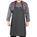 A man wearing a Uncommon Chef pinstripe denim bib apron with burgundy accents and 3 red pockets.