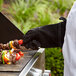 A person in Outset black leather gloves cooking food on a grill.