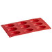 A red silicone baking tray with nine Madeleine compartments.