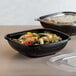 Two Fineline black plastic bowls filled with pasta and vegetables.