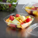 A Fineline clear plastic bowl filled with fruit with a plastic lid.