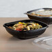 Two black Fineline plastic bowls filled with pasta and vegetables.