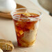 A clear Fabri-Kal customizable plastic cup filled with iced tea and ice cubes next to cookies.