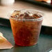 A Fabri-Kal Kal-Clear plastic cup filled with ice and brown soda on a tray.