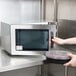 A person using a Panasonic commercial microwave to heat food on a plate.