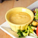 A yellow Festiware ramekin filled with yellow sauce next to a green salad.