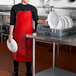 A person wearing a red San Jamar EZ-KLEEN apron in a kitchen holding a white plate.
